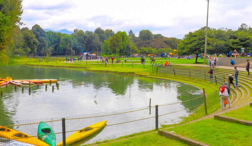 Lago artificiale nel Parco Simón Bolívar di Bogotà, con varie persone tutte intorno, circondato da alberi e con canoe sulla superficie, sotto un cielo nuvoloso