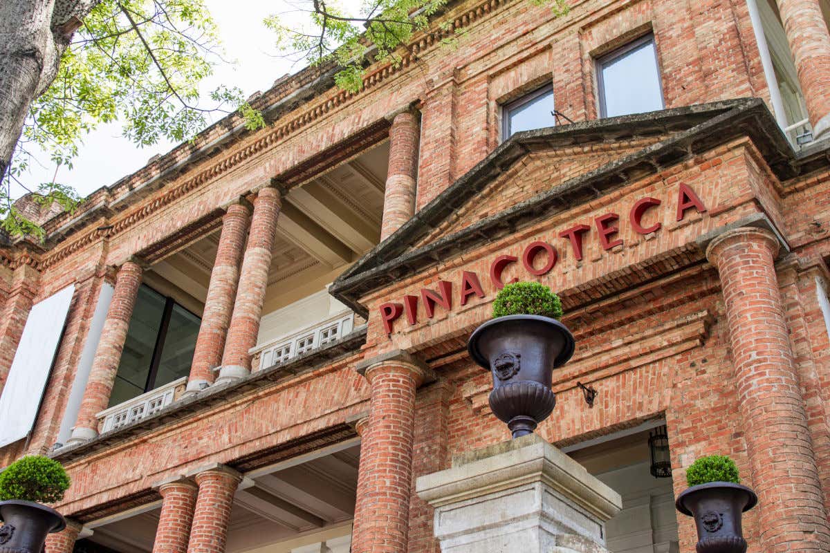 Fachada de tijolos da Pinacoteca do Estado de São Paulo vista de baixo. Acima, é possível ver algumas árvores do Parque Jardim da Luz