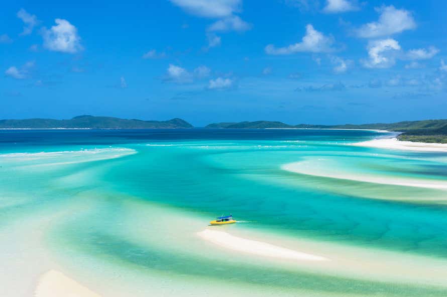 Una barca naviga in acque turchesi, frastagliate da banchi di sabbia delle isole Whitsunday, in Australia