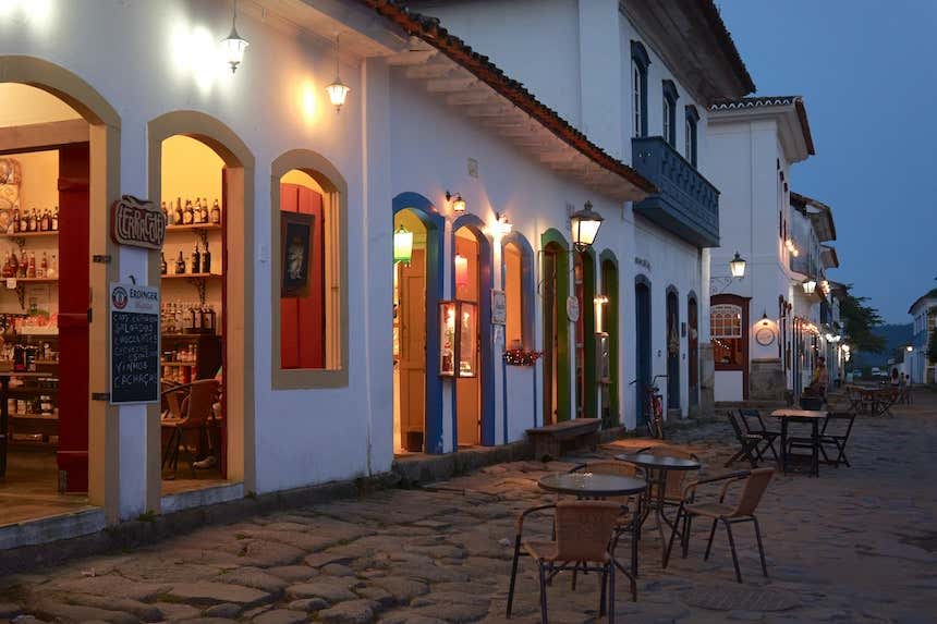 Bar que funciona em um edifício colonial do centro histórico de Paraty com mesas na calçada ao anoitecer