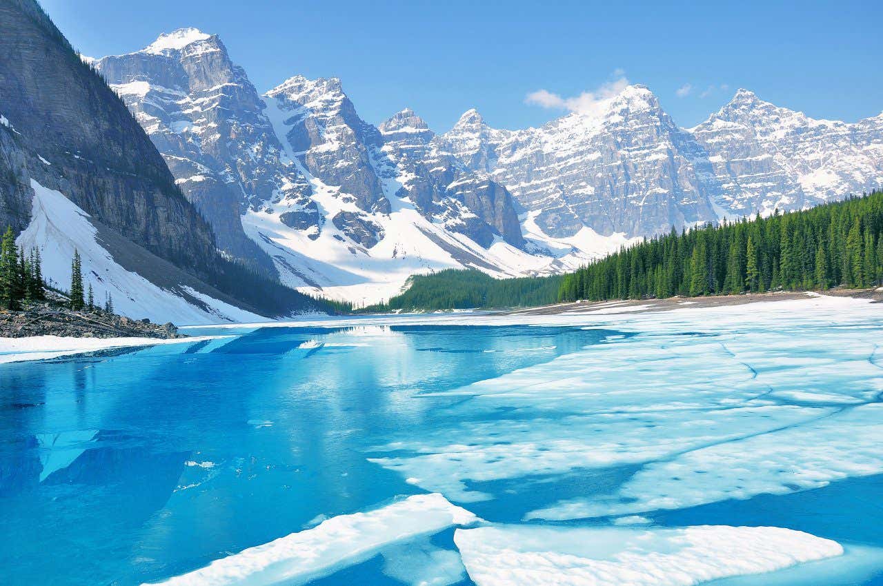 Lac glacé entouré de montagnes enneigées et d'arbres