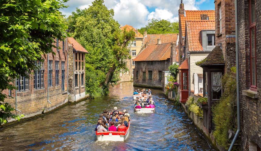 Tre barche con passeggeri a bordo su uno dei canali di Bruges passano accanto a varie case della città