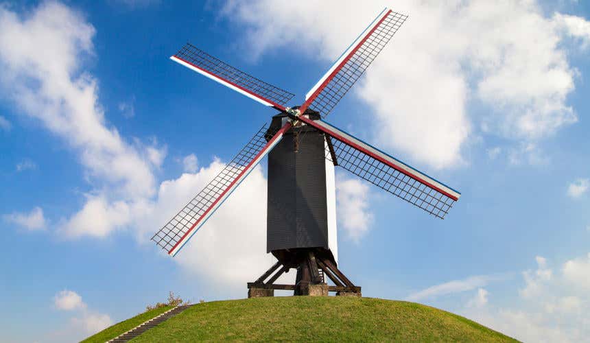 Sint-Janshuismolen, il mulino di San Giovanni, bianco e nero con eliche rosse su una collina verde di Bruges