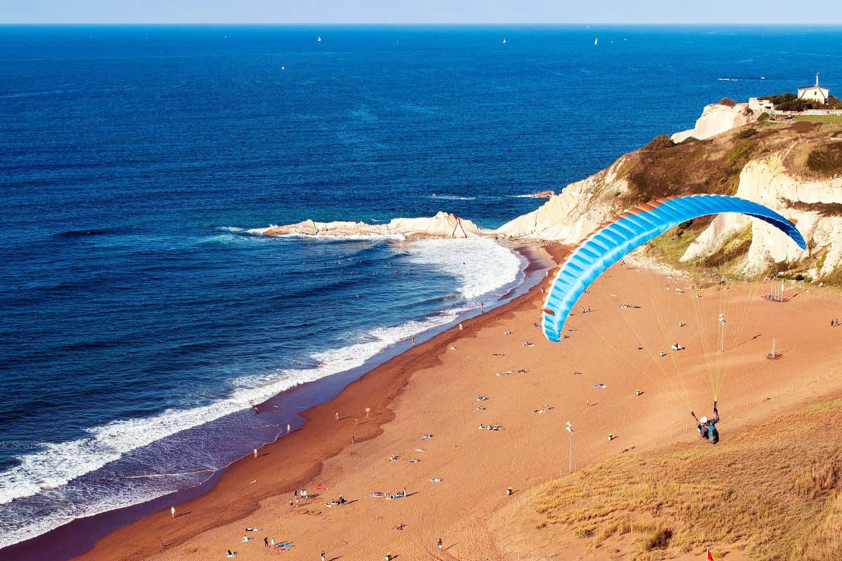 A paraglider flying over the Basque Coast in the municipality of Sopelana on a clear day with calm sea.