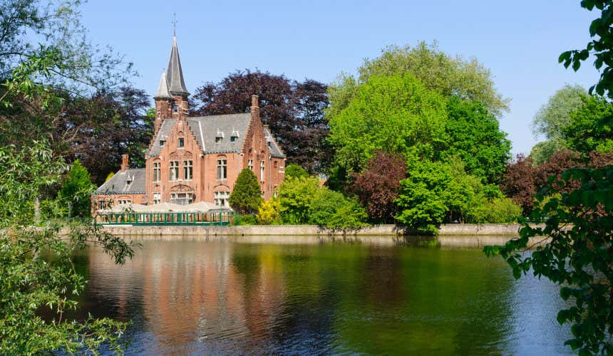 Lago dell'Amore nel Parco Minnewater di Bruges, con un piccolo edificio e alti alberi lungo le sponde