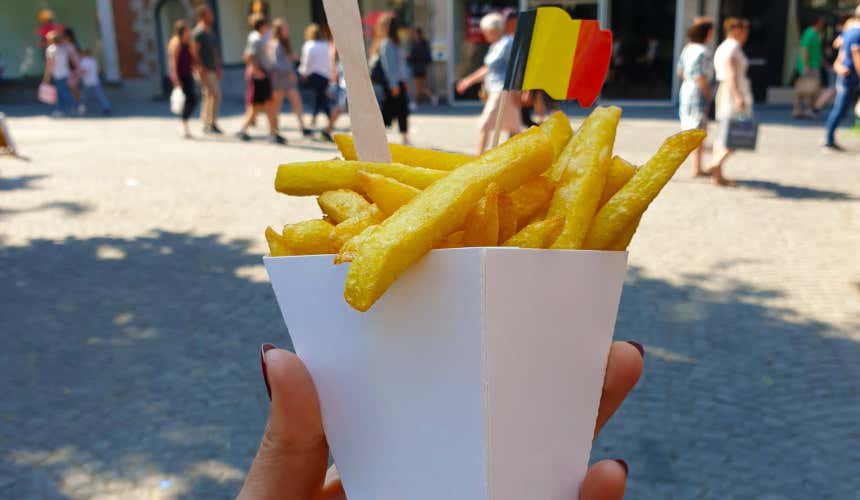 Ragazza regge delle patate fritte con bandierina del Belgio e alcune persone camminano sullo sfondo lungo una strada