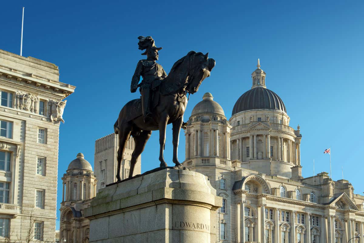 Scultura equestre del re Edoardo VII di fronte a uno degli edifici del porto di Liverpool con la bandiera britannica sullo sfondo