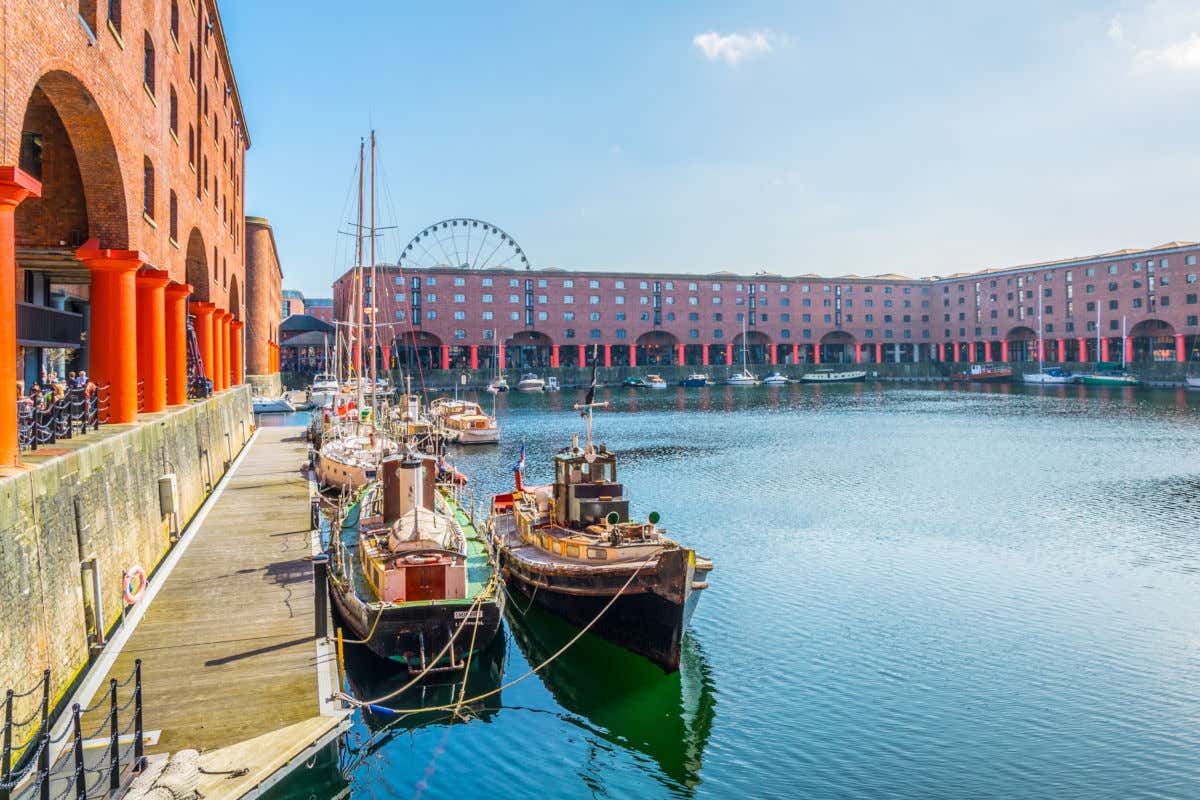 Alcune piccole barche attraccate alla Royal Albert Dock, la darsena di Liverpool, e serie di edifici in mattoni degli antichi magazzini portuali della città sullo sfondo