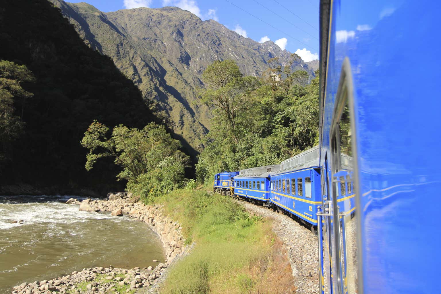 Il treno blu di Machu Picchu accanto a un corso d'acqua circondato da montagne