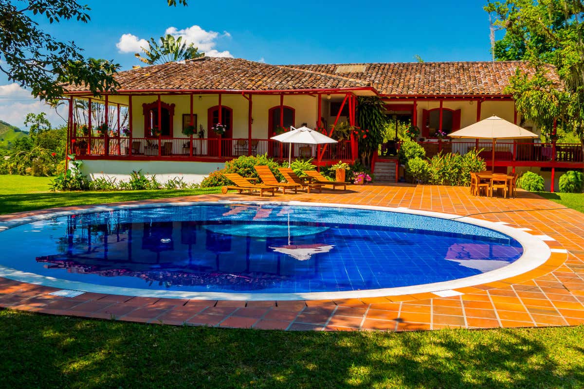 Piscina y fachada de una hacienda tradicional del Eje Cafetero de Colombia con sus techos de teja y sus llamativas puertas rojas