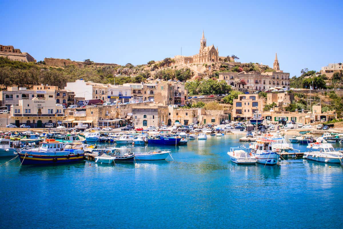 Puerto pesquero y varias casas en una ciudad de Gozo, coronada por una iglesia en los alto de una pequeña colina