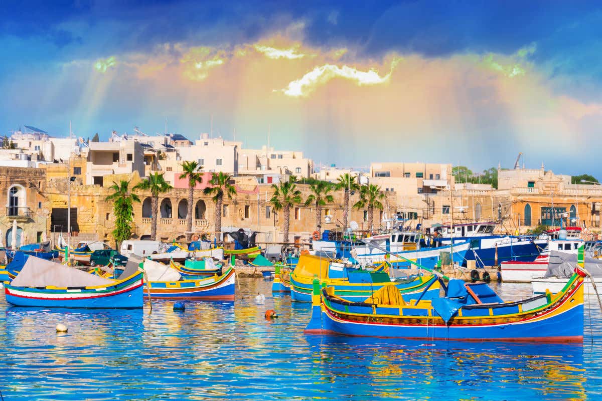 Barcos coloridos a la luz del atardecer junto a varias casas en el pequeño pueblo pesquero de Marsaxlokk, en un día nublado de Malta