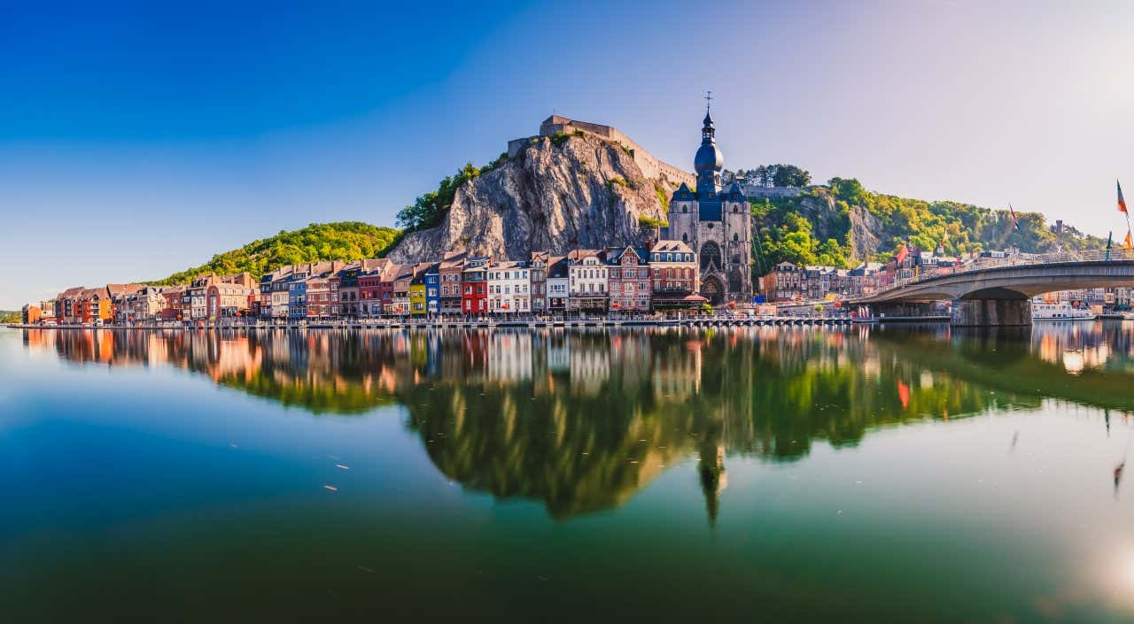 Vue sur la ville de Dinant reflétée dans l'eau et surplombée par une grande falaise