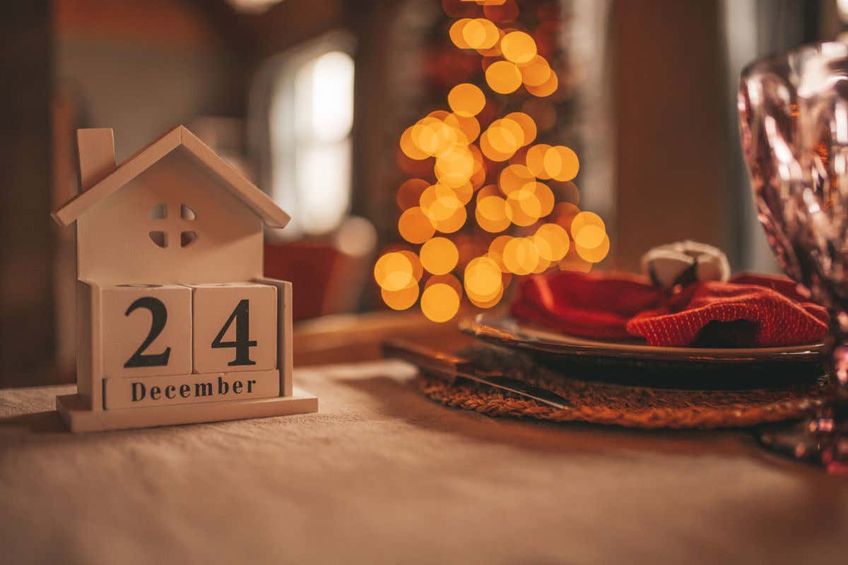 A wooden table decorated with a calendar in the shape of a little house marking 24 December, Christmas Eve Day.