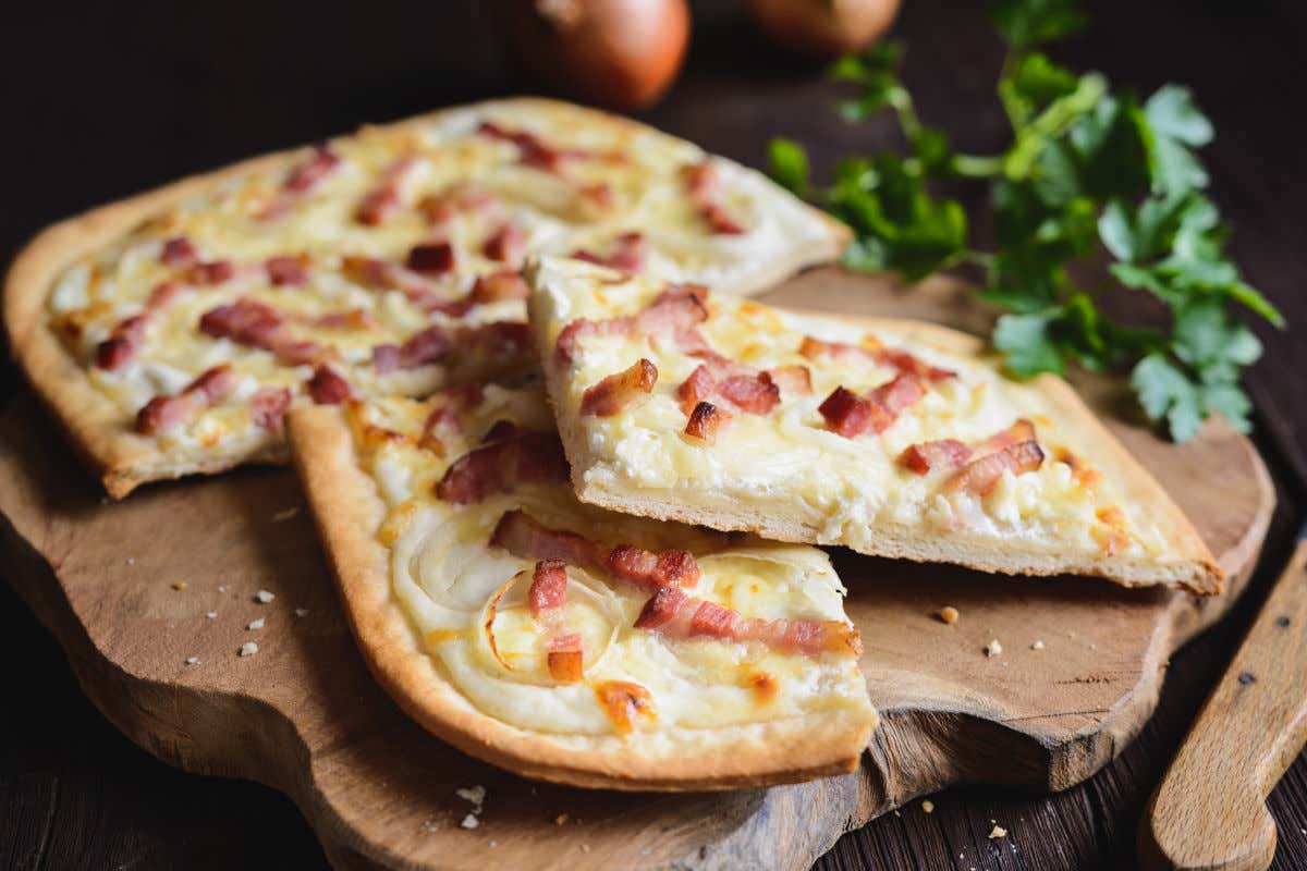 Una tabla de madera con una tarte flambée, una pizza alsaciana de masa fina con bacon y cebolla