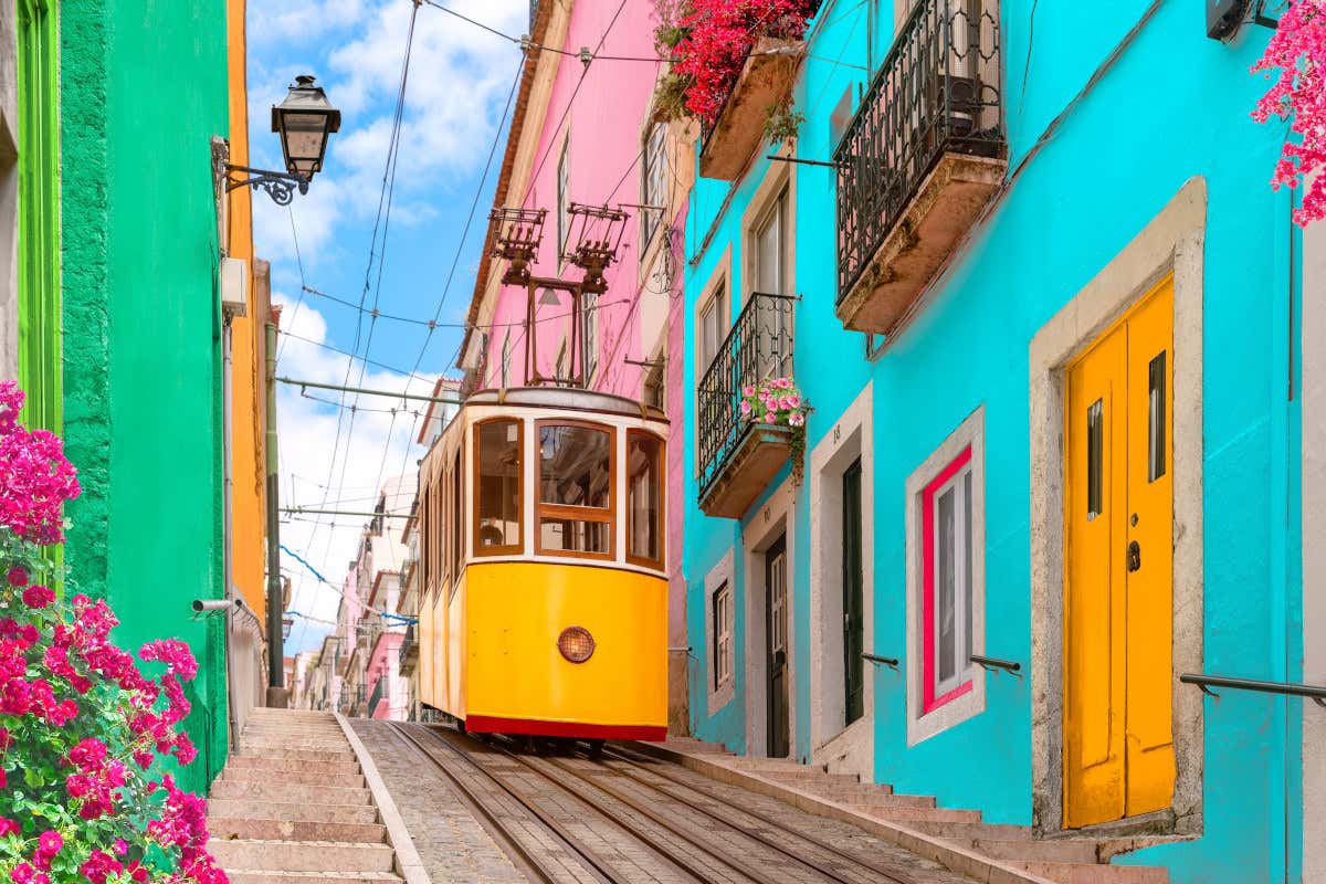 Un tranvía amarillo subiendo por una calle en pendiente con varias casas de colores en Lisboa