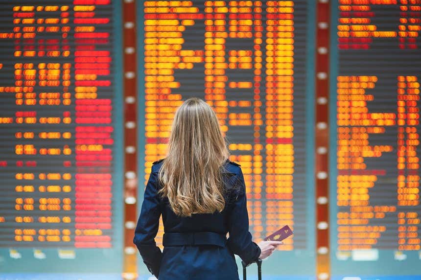 Une femme regardant la liste des destinations dans un aéroport avec son passeport prêt pour voyager