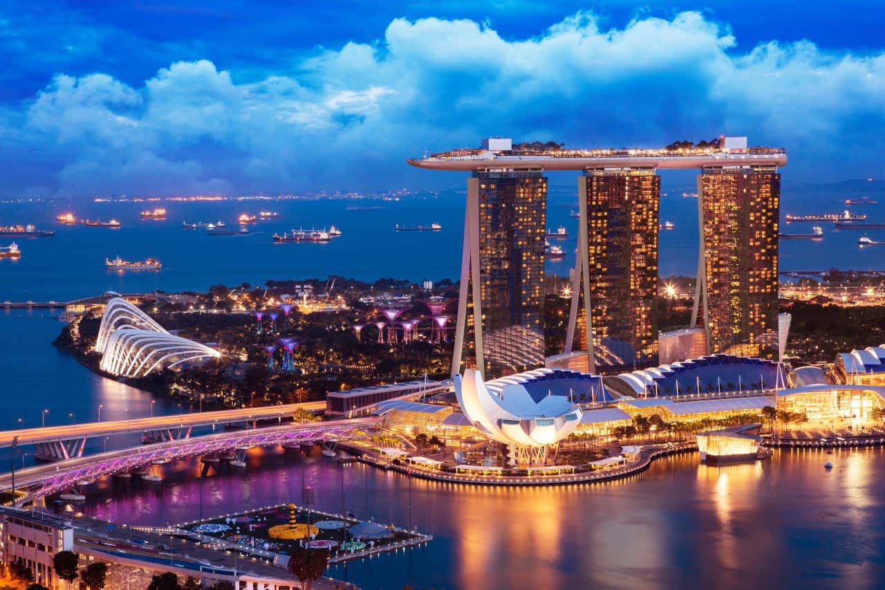 Edifici illuminati a Singapore al tramonto con diverse barche tutte intorno sotto un cielo nuvoloso