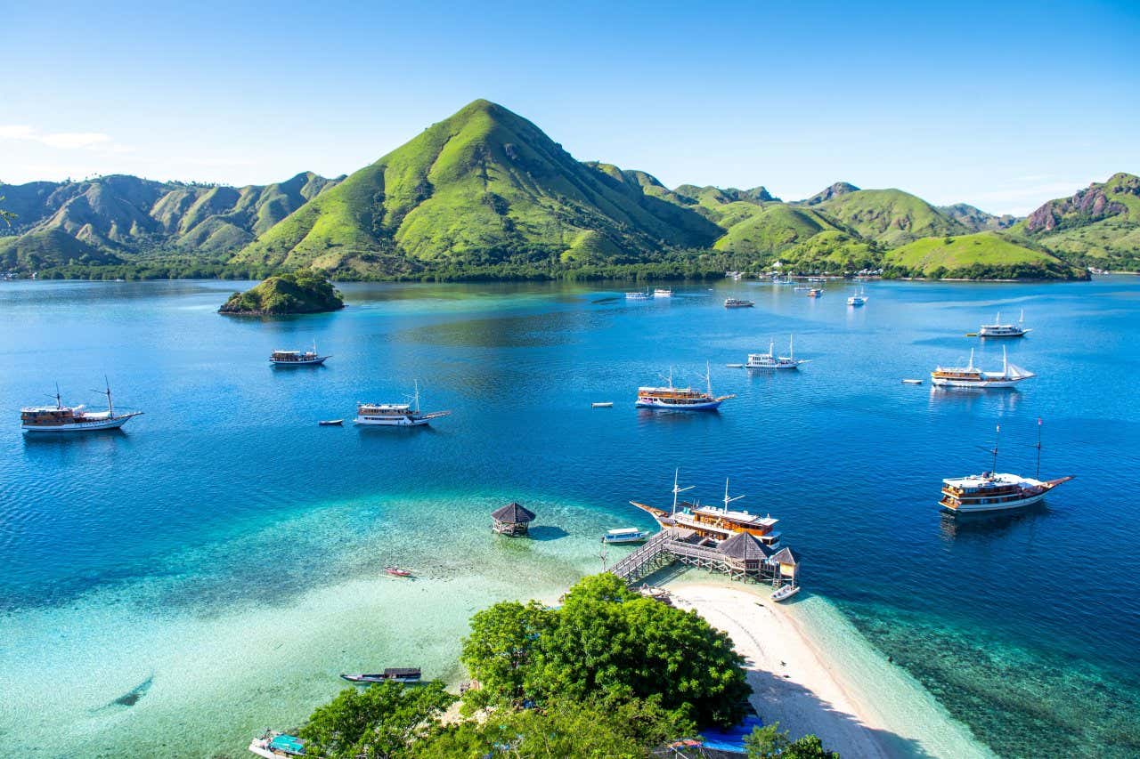 Vista panoramica sull'isola di Kelor in Indonesia, con alcune barche nelle acque che la circondano e un paesaggio verde e collinare all'orizzonte