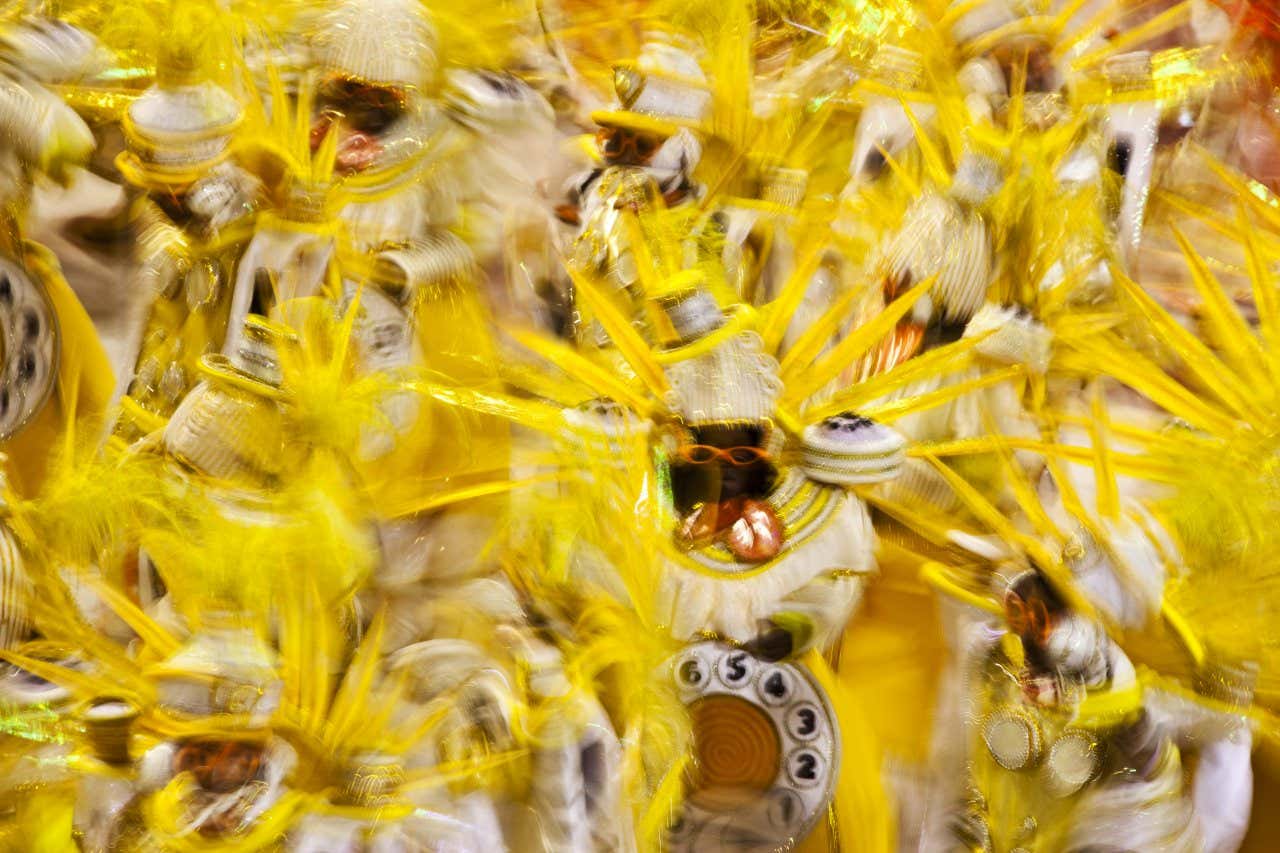 Várias pessoas com fantasias brancas e amarelas em uma ala de uma escola de samba do Carnaval do Rio de Janeiro