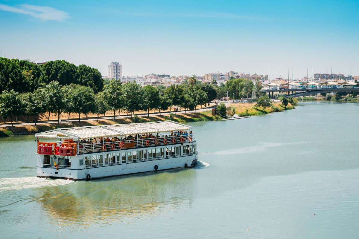 Un barco de dos pisos navegando por el río Guadalquivir frente a un puente