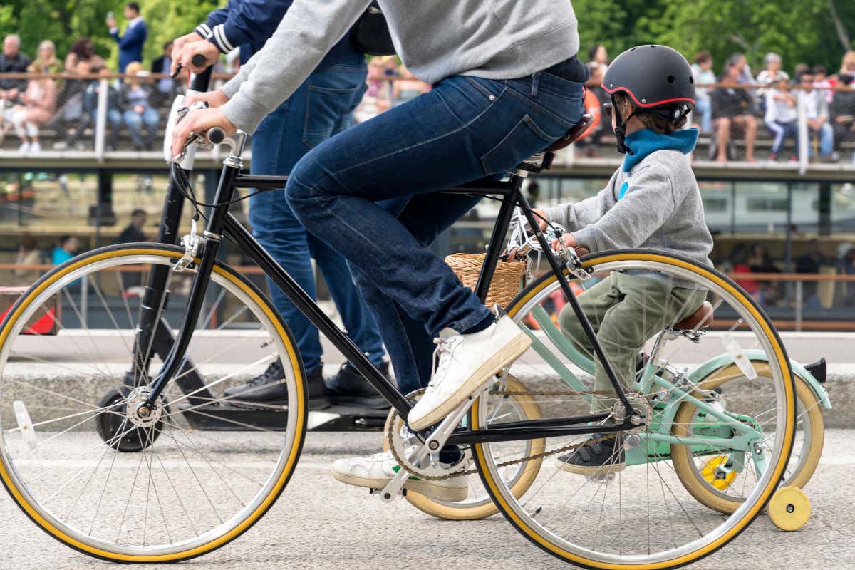 Un uomo pedala con il figlio lungo una strada asfaltata vicino a un fiume