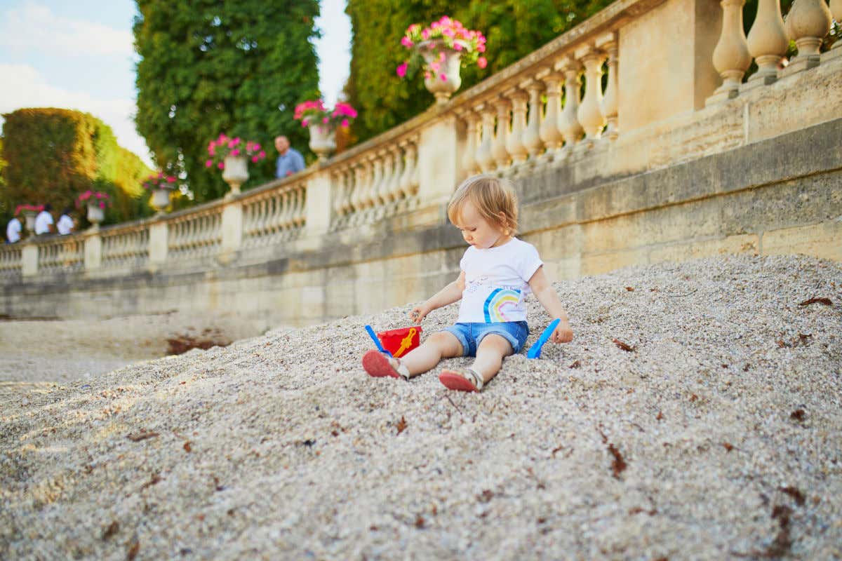 Una bambina di circa due anni seduta su un cumulo di sabbia in un parco di Parigi