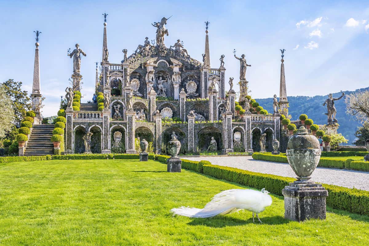 Un pavo real de color blanco frente a un conjunto escultórico en unos jardines