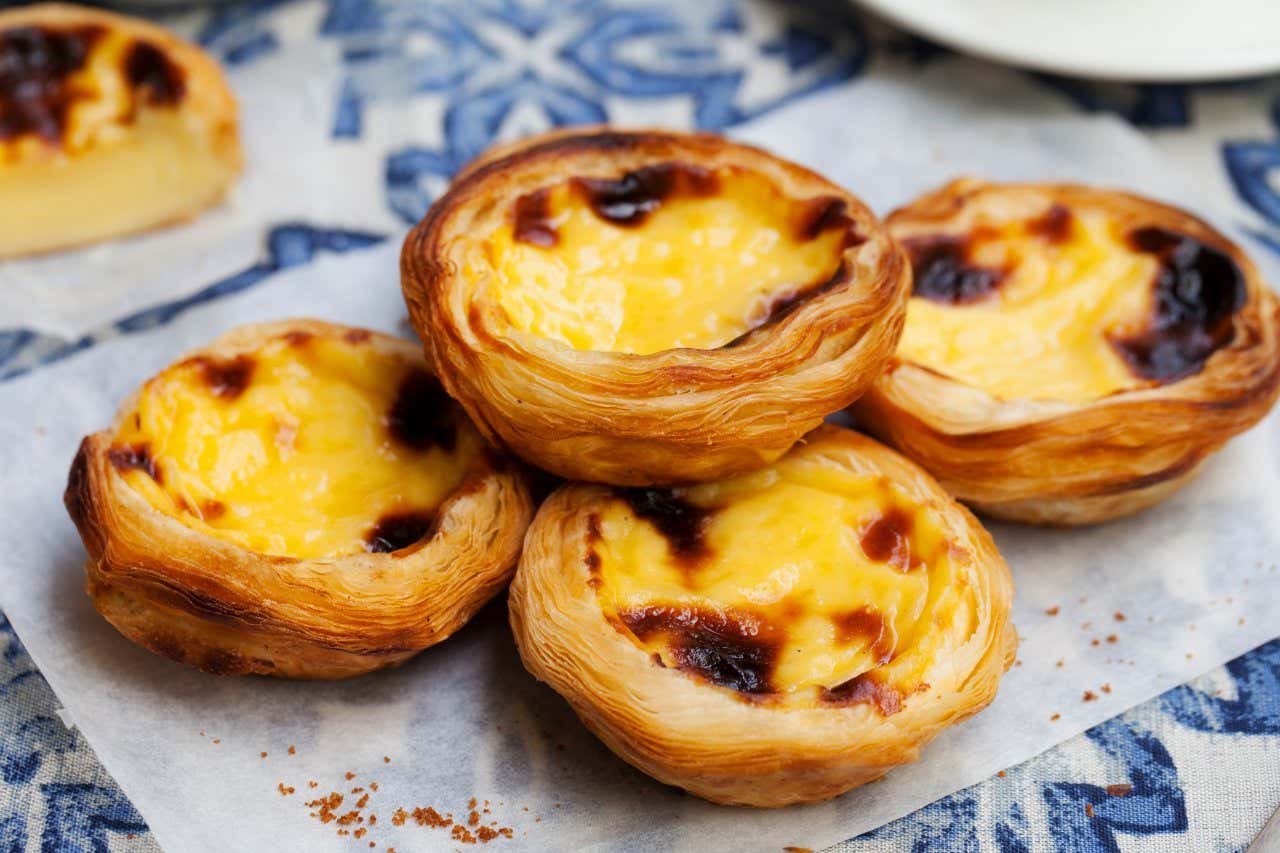 4 Pastel de natas on a blue and white tablecloth.