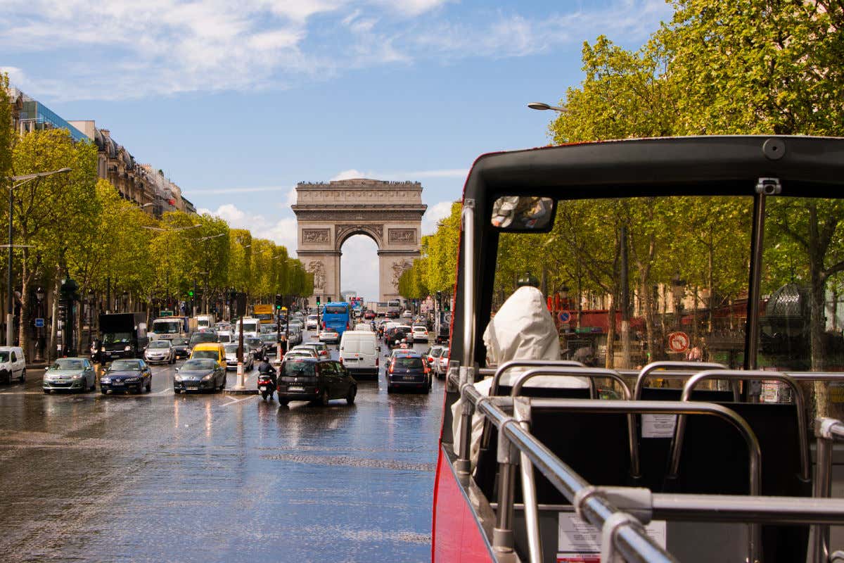 Primo piano di un autobus decappottabile che percorre gli Champs Elysées con l'Arco di Trionfo in lontananza