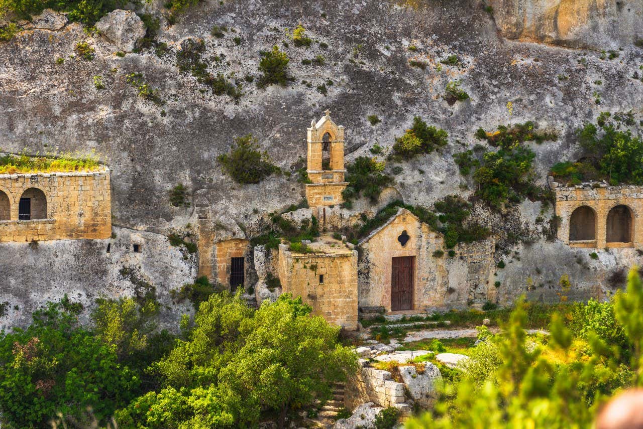 La facciata di una piccola chiesa in mattoni affiora dalla parete rocciosa nella Murgia Materana, una meta naturalistica perfetta per Pasqua e Pasquetta