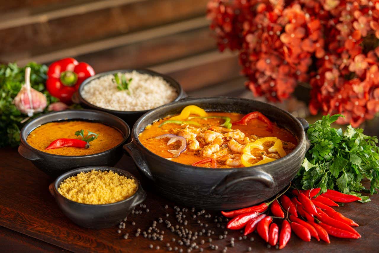 Prato de moqueca de camarão servido com arroz, pirão e farinha de mandioca e pimentas decorativas.