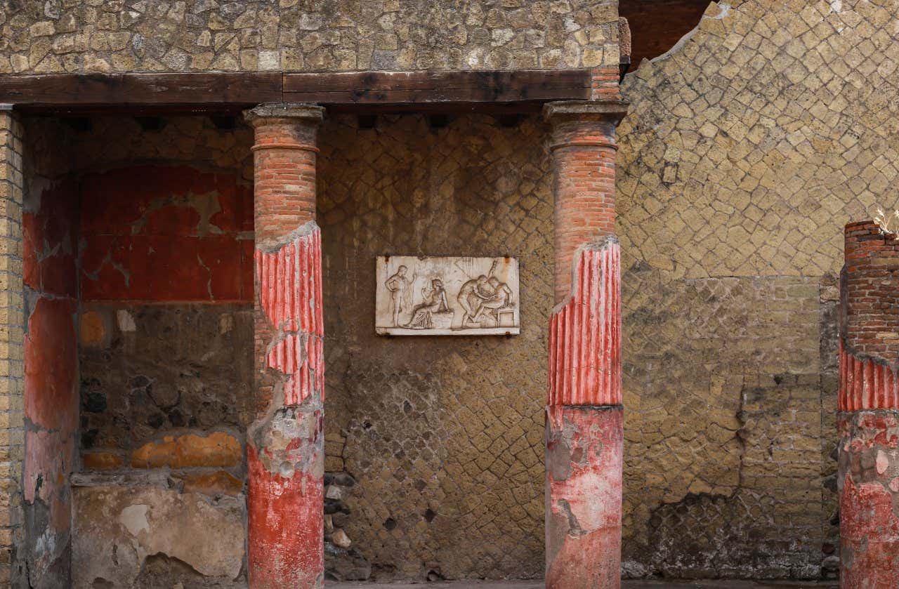 Un portico con un bassorilievo romano in marmo tra due colonne rosse a Ercolano