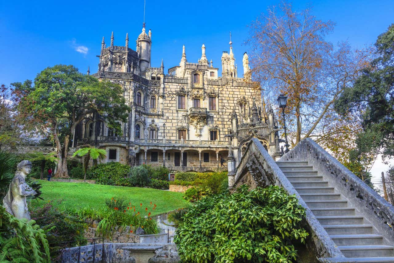 The façade of the Quinta da Regaleira Palace in Sintra surrounded by greenery and a staircase in front.