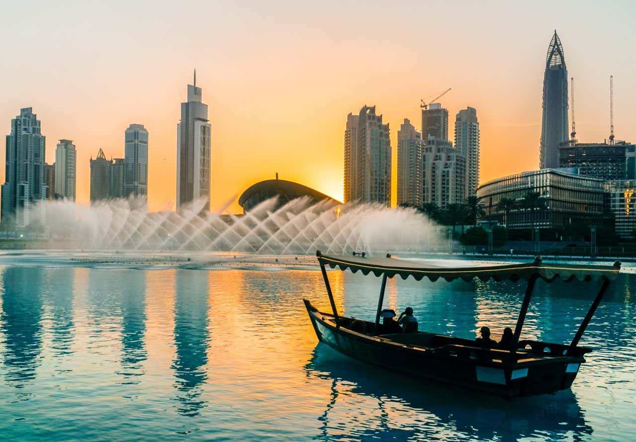 A boat sailing in Dubai, with the city's skyline in view at sunset. 