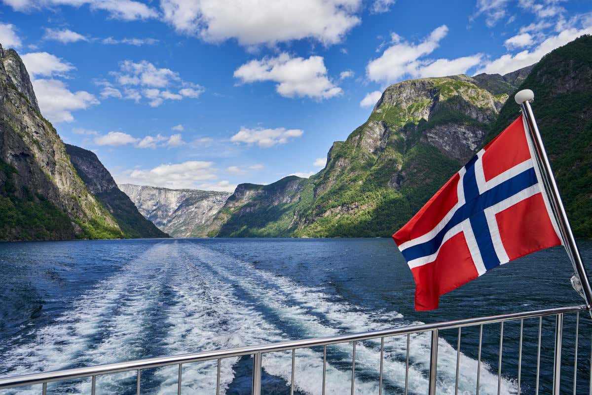 Ringhiere a poppa di una nave con bandiera norvegese mentre naviga in uno dei fiordi norvegesi tra alte montagne
