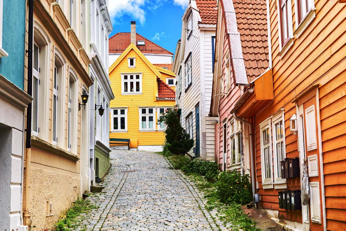 Una strada acciottolata di Bergen fiancheggiata da case in legno color pastello in una giornata limpida
