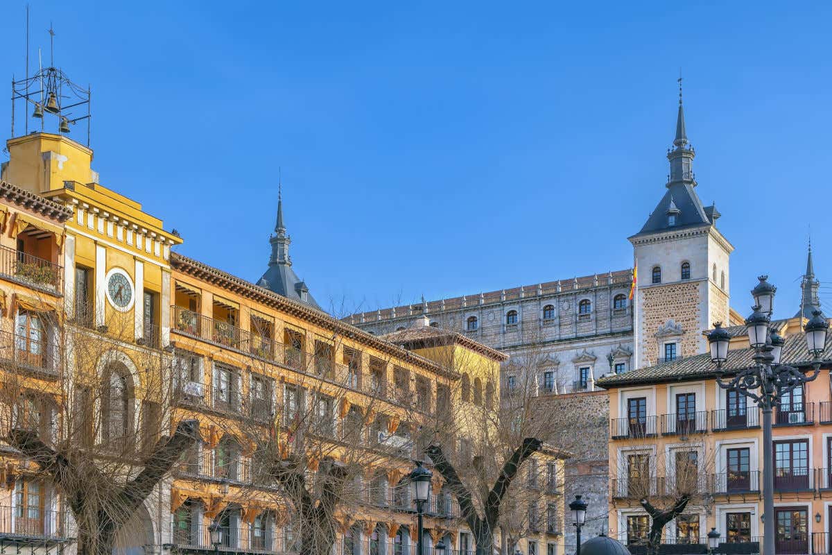 Edifici nella Plaza de Zocodover di Toledo con alcuni alberi senza foglie e le due torri dell'Alcázar sullo sfondo