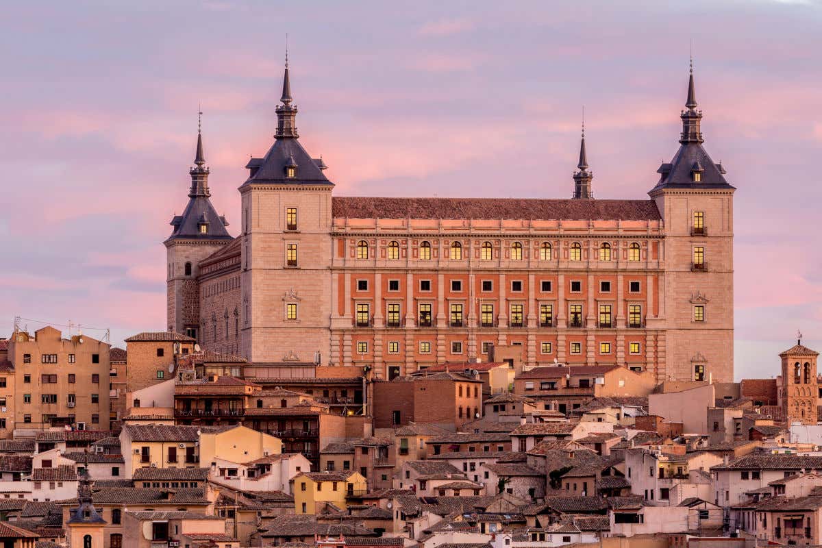 Facciata dell'Alcázar di Toledo, poco decorata, accanto ad alcune case del centro storico al tramonto