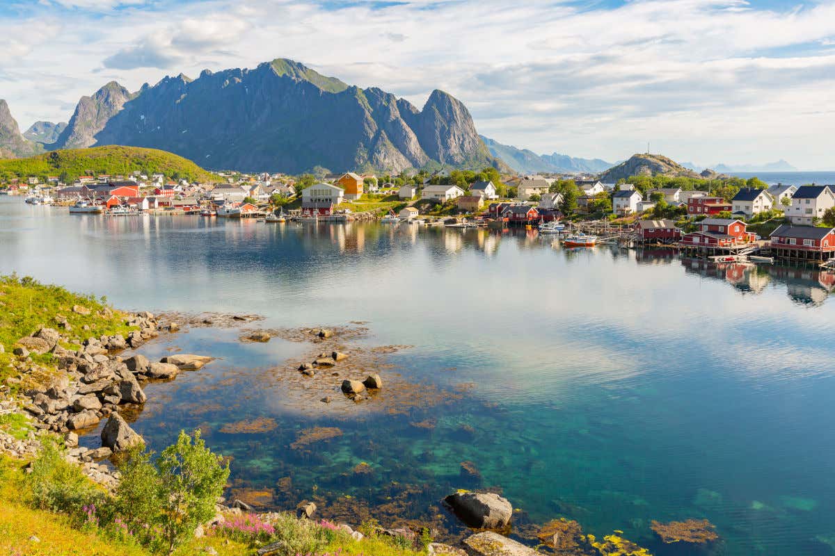 Small red and white wooden houses on the shore of a Norwegian Fjord with rocky mountains behind