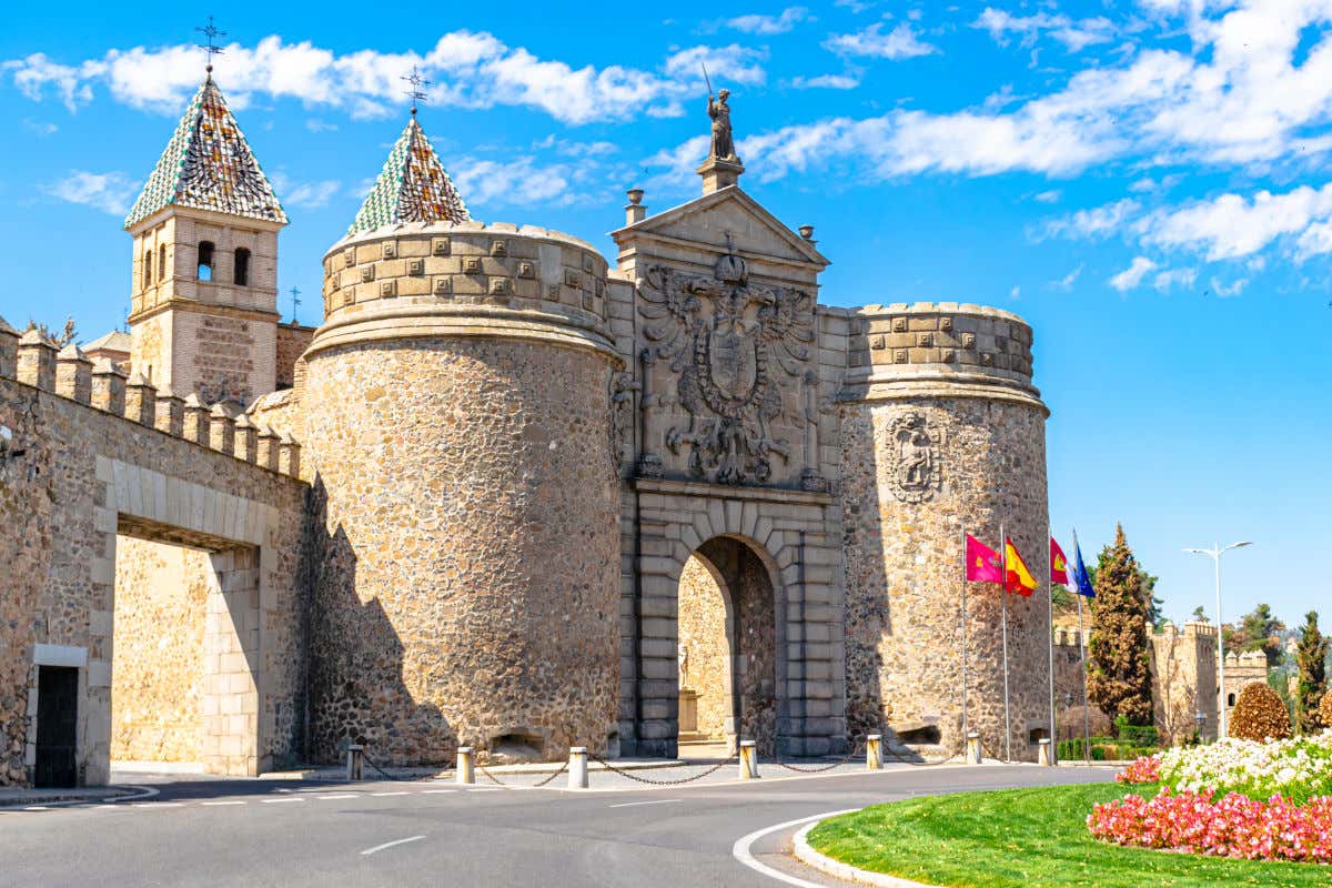 La Porta di Bisagra, un portico monumentale con un enorme scudo di pietra davanti a una rotonda e diverse bandiere