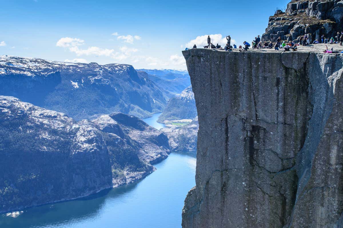 Turisti in cima a una rupe con vista sulle montagne innevate della Norvegia e su un fiordo