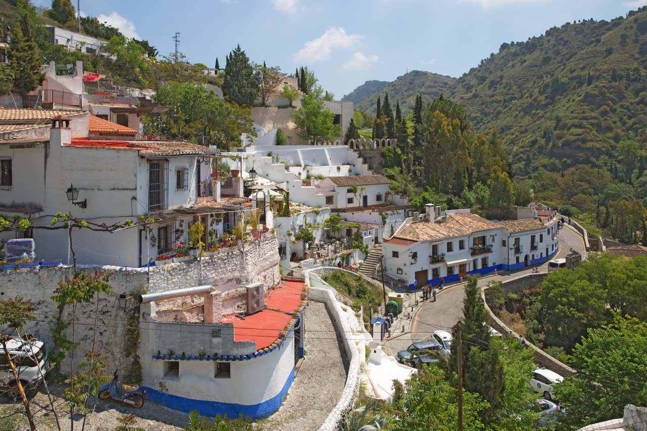 An aerial shot of Sacromonte in Granada, with its empty streets in the foreground and rolling forested hills in the background.