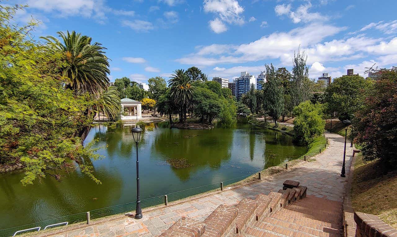 A central park in Montevideo with a large pond and various types of green trees