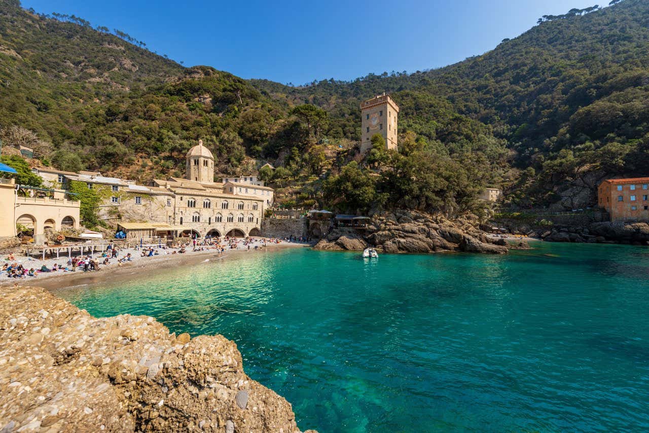 La piccola spiaggia di San Fruttuoso con il monastero che poggia sulla collina e alcuni bagnanti