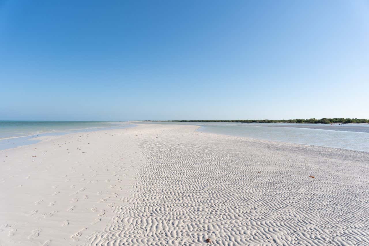 A white stip of sand surrounded by water under a blue sky