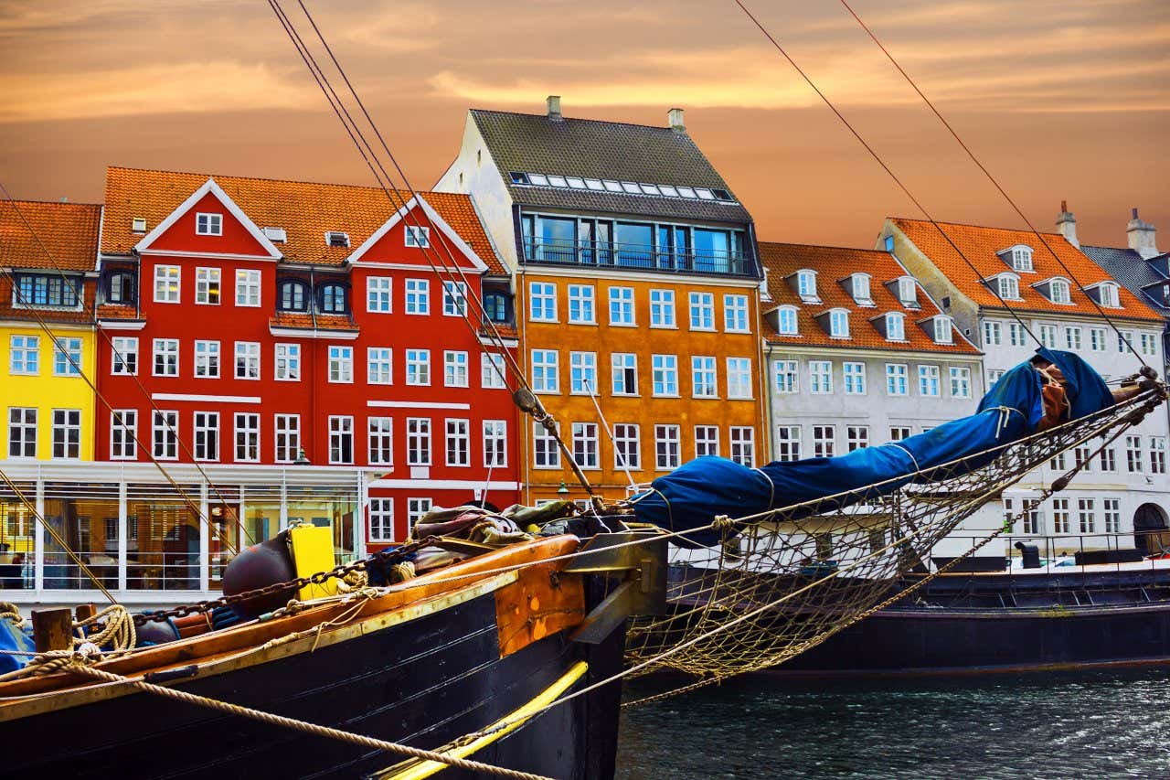 Red, yellow, orange and white tall buildings on a canal front with a close-up of a wooden sailing boat in the water in Copenhagen.