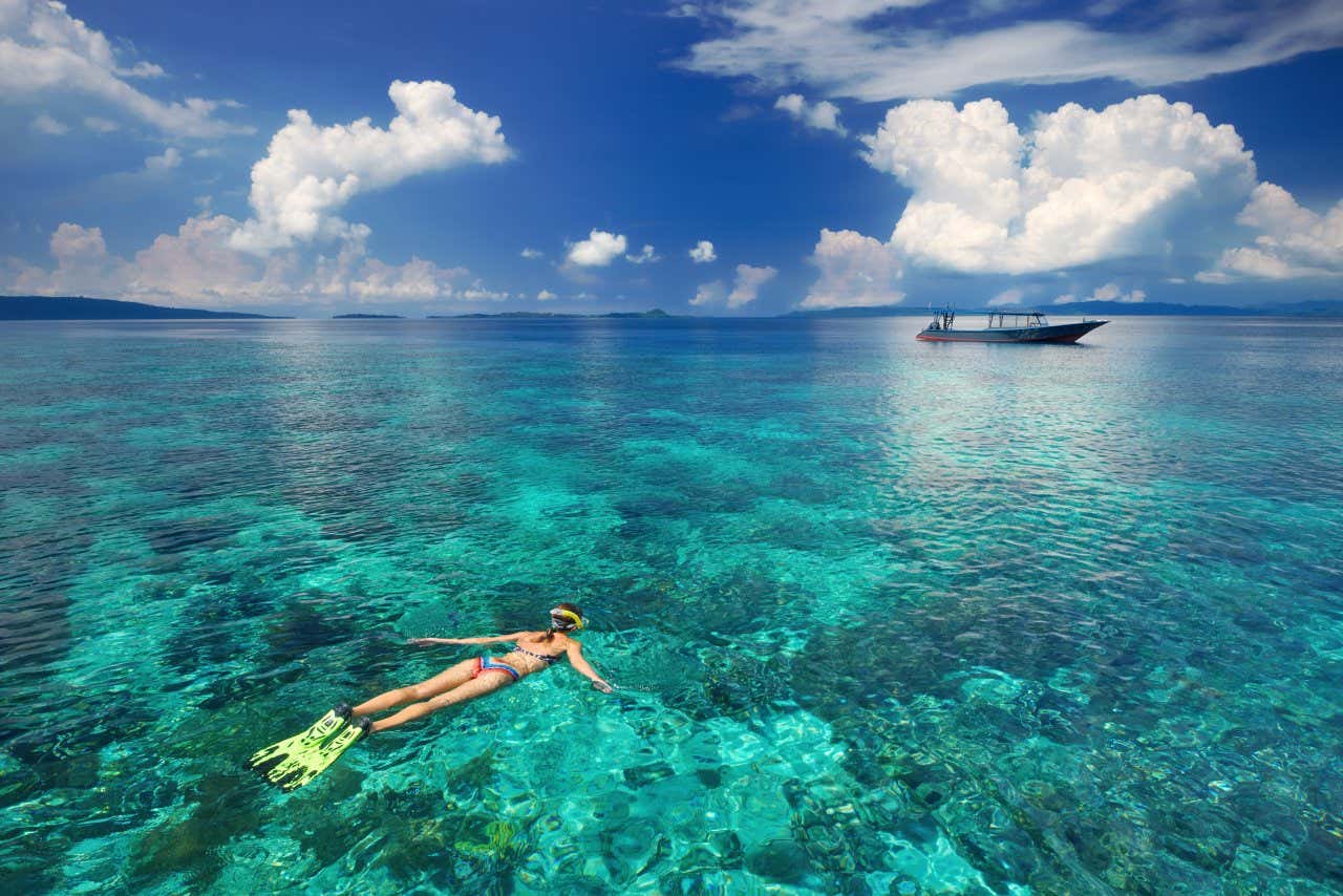 Una donna fa snorkeling in mare aperto vicino a una piccola barca