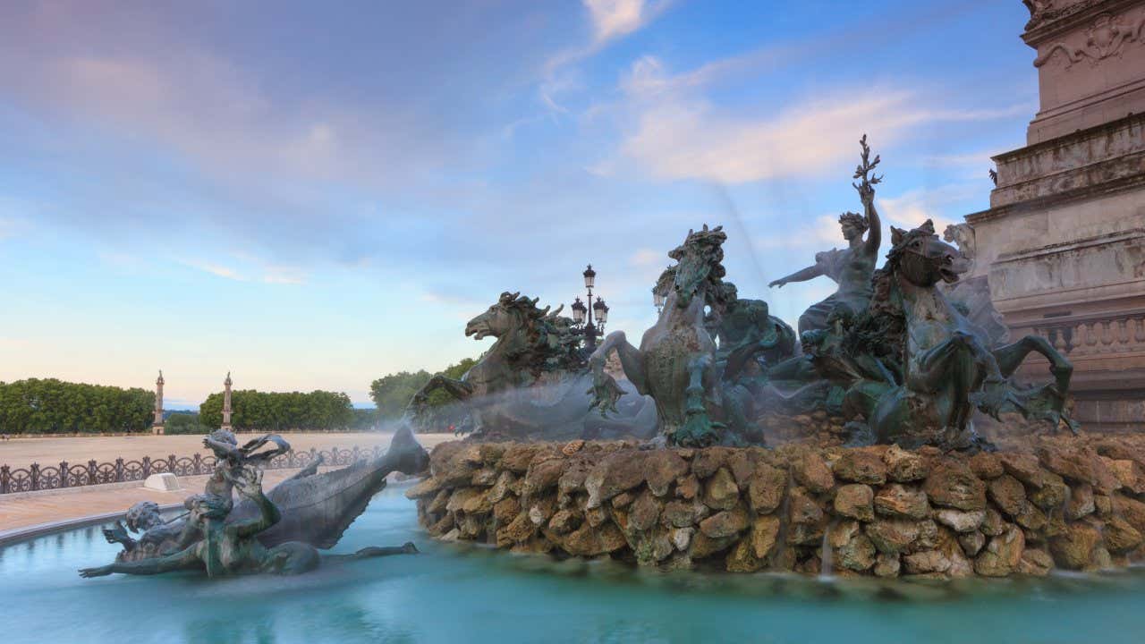 A bronze sculpture of men and horses in action, water spraying from the sculpture that sits at the bottom of an obelisk in the middle of Place des Quinconces