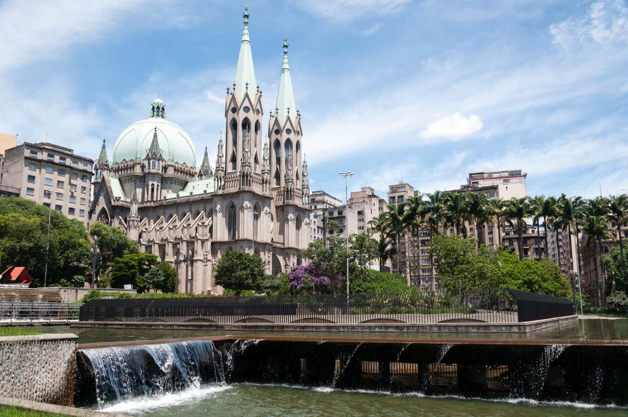 Vista sulla La Cattedrale Metropolitana di San Paolo, con la sua architettura gotica, accanto a un canale con una diga e con varie palme di fronte